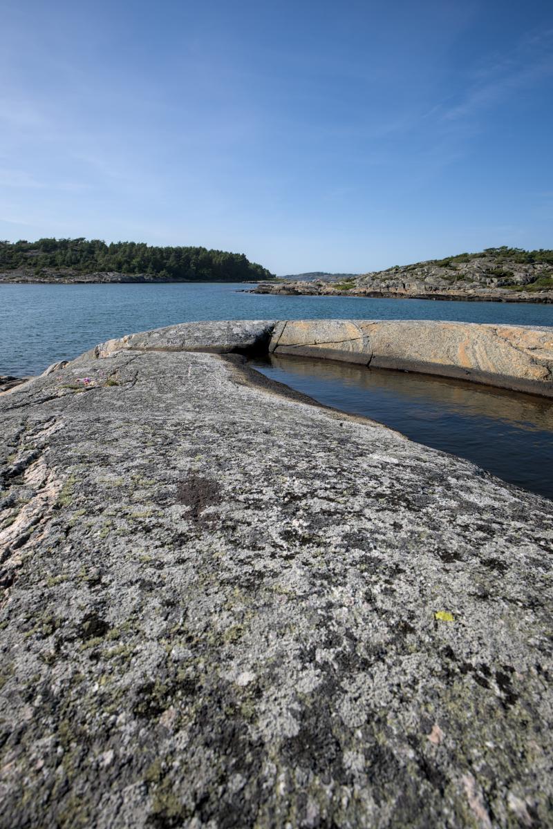 I förgrunden finns en pöl i en klippa. Lite längre bort och nedanför ligger havet. Bakom det syns två landmassor. Den ena är en ö, den andra fastland.