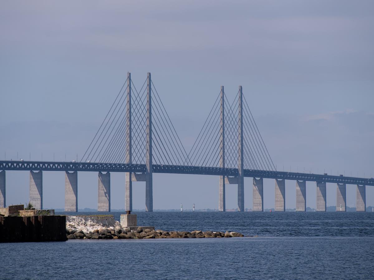 Auf diesem Bild ist die Öresundsbron mit Kopenhagen im Hintergrund zu sehen. Das Bild wurde von Malmö aus aufgenommen, und im Vordergrund sind einige Steine zu erkennen.