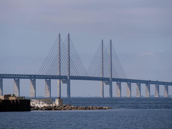 Auf diesem Bild ist die Öresundsbron mit Kopenhagen im Hintergrund zu sehen. Das Bild wurde von Malmö aus aufgenommen, und im Vordergrund sind einige Steine zu erkennen.