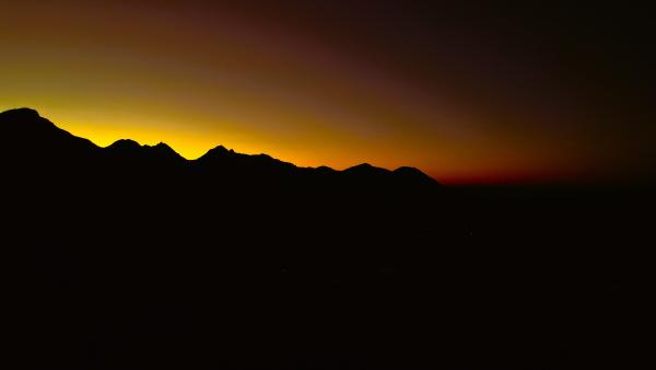 Die Sonne geht in goldenem Glanz unter und lässt Bäume als Silhouetten vor einem leuchtenden Himmel erscheinen.