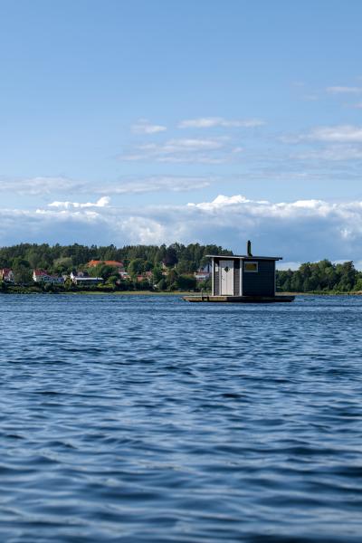 Eine schwimmende Sauna auf einem schwedischen See. Im Hintergrund stehen einige Bäume und Häuser.