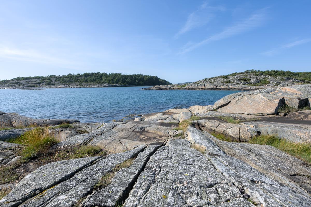Ein felsiger Strand an der schwedischen Westküste. Im Hintergrund sind Land und eine Insel zu sehen. Dazwischen liegt das Meer.