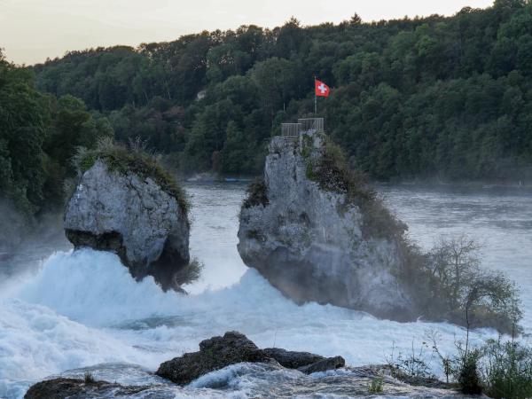 Foto des Rheinfalls in der Schweiz. Auf der Spitze eines Felsens im Wasser steht eine Schweizer Flagge.