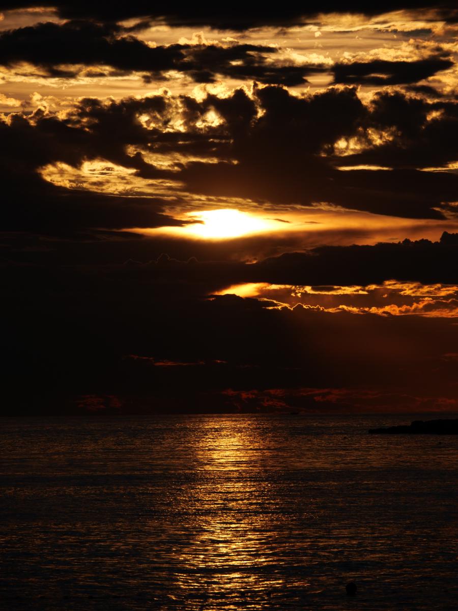 Goldene Strahlen des Sonnenuntergangs, die über dem Meer durch die Wolken brechen.