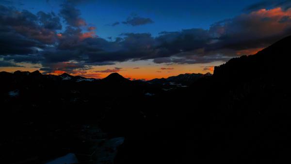 Sonnenuntergang über den Alpen mit orangefarbenen und violetten Tönen am Himmel.