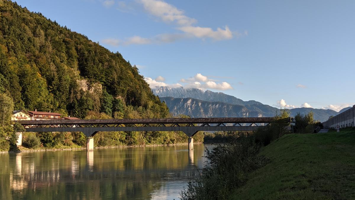 Eine Holzbrücke, die einen ruhigen Fluss überquert, mit Bergen in der Ferne.