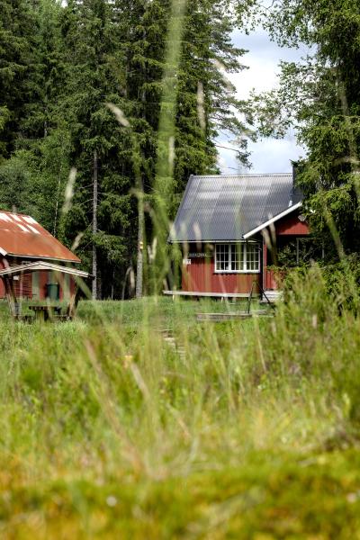 Ein rotes nordisches Haus mit einigen Picknickmöbeln im Freien. Im Vordergrund ist Gras, im Hintergrund ein Wald.