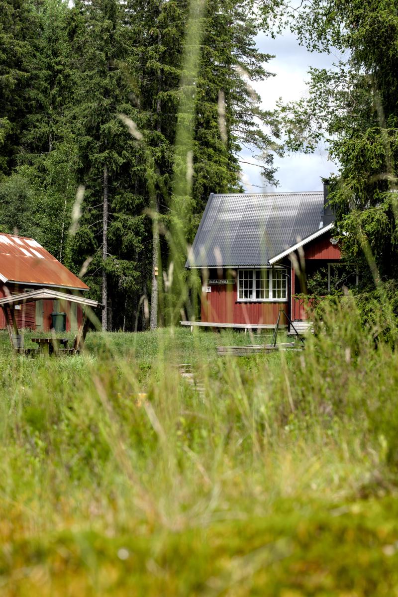 Ein rotes nordisches Haus mit einigen Picknickmöbeln im Freien. Im Vordergrund ist Gras, im Hintergrund ein Wald.