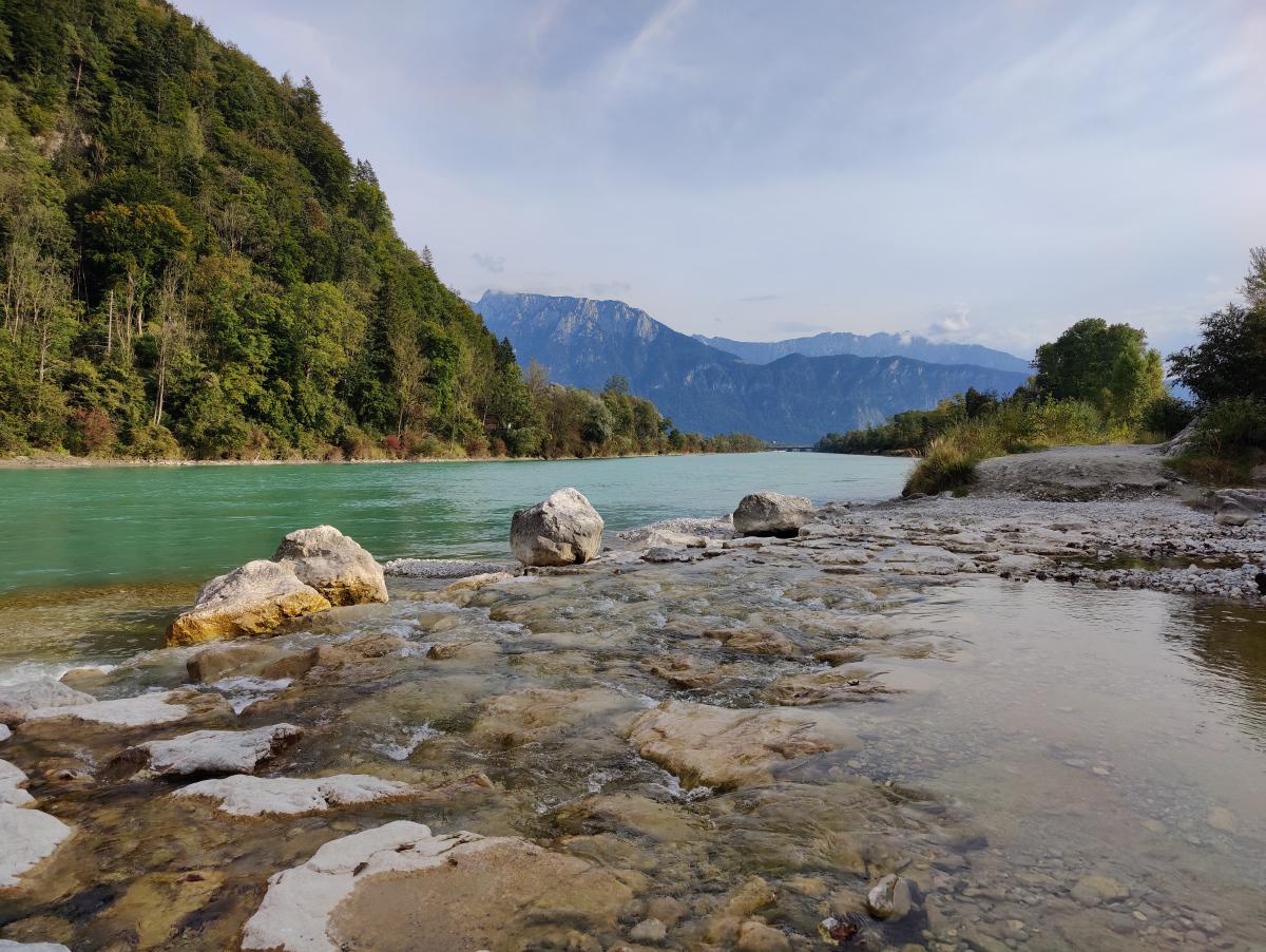 Ein klarer, ruhiger Fluss mit Steinen und einer Bergkulisse.