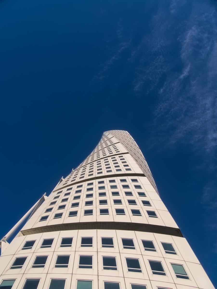 Ein Foto des Turning-Torso-Gebäudes in Malmö mit blauem Himmel im Hintergrund. Das Foto wurde von unterhalb des Turms in Richtung Himmel aufgenommen.
