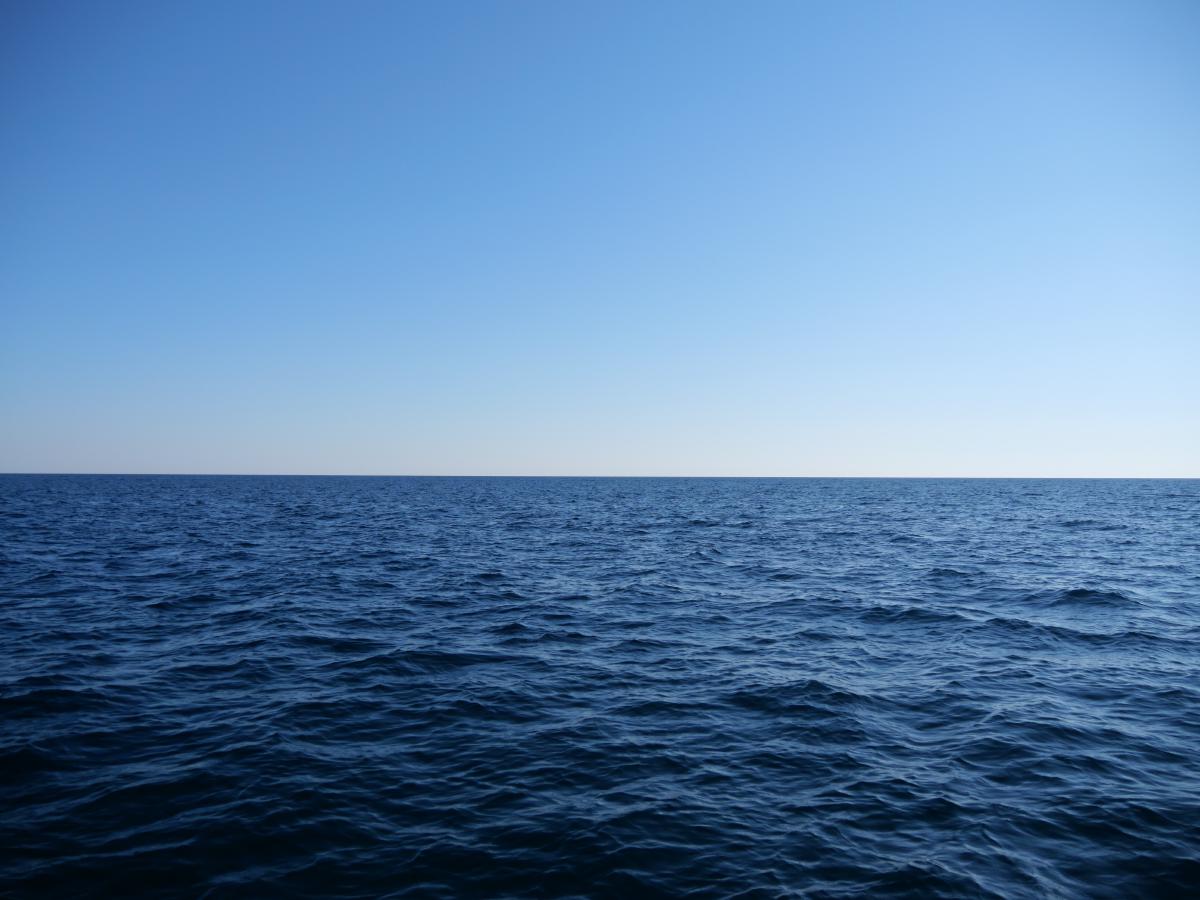 Ein friedlicher Blick auf das Meer, dessen Wasser sich unter einem klaren blauen Himmel bis zum Horizont erstreckt.