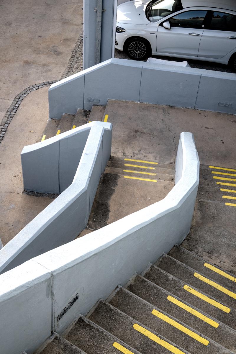 Das Bild zeigt eine Treppe im Freien, die zu einem Parkplatz hinabführt. Die Stufen haben leuchtend gelbe Streifen.